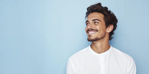 Portrait of a cheerful young man with a joyful smile and stylish hair against a blue background.