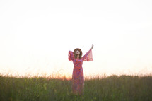 a woman in a pink dress walking through a field with arms raised 