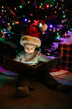 a boy reading a book under a Christmas tree 