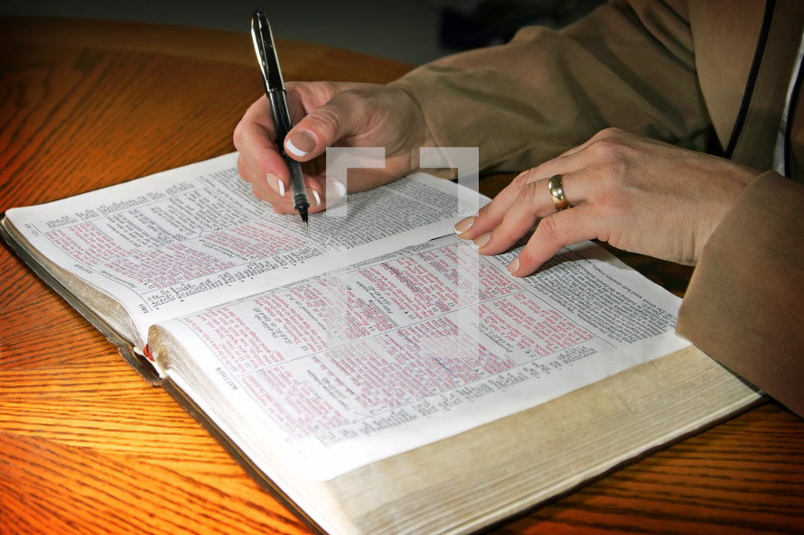A professional woman studies the Holy Bible during some quiet time set aside in her day - focus point on the woman's hands.