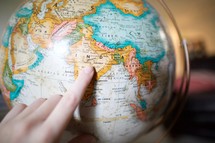 a finger pointing to India on a globe 