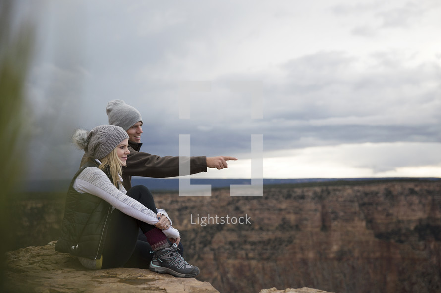 happy couple sitting on a mountaintop looking out. 