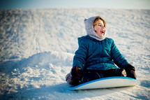 child sledding down a snow covered slope