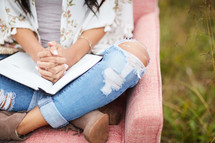 a young woman sitting in a chair in a field reading a Bible and praying 
