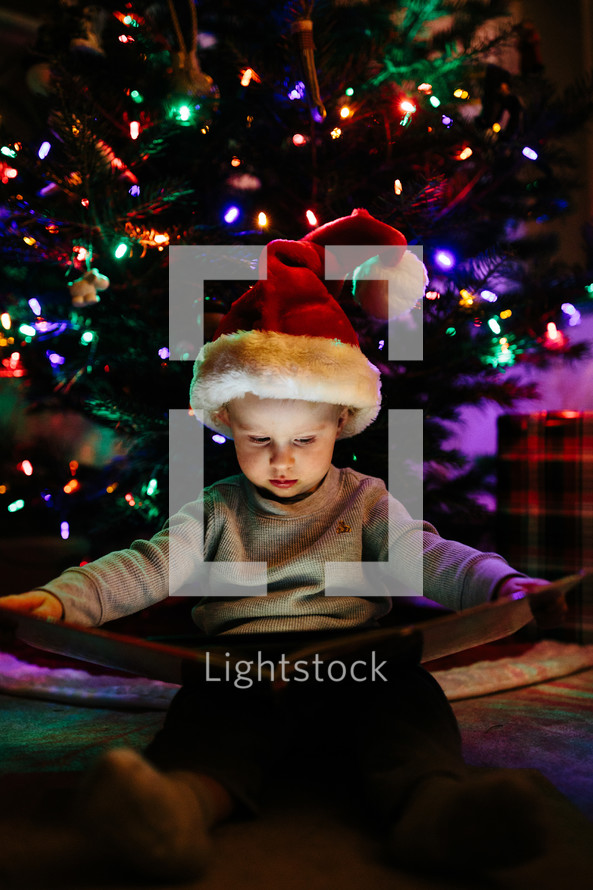 a child reading a book under a Christmas tree 