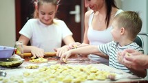 Family cooking in kitchen. Boy learn to make dough pies. Mom, grandmother and daughter skillfully make products from fresh dough. They have a lot of fun together. Family preparing pie dough.