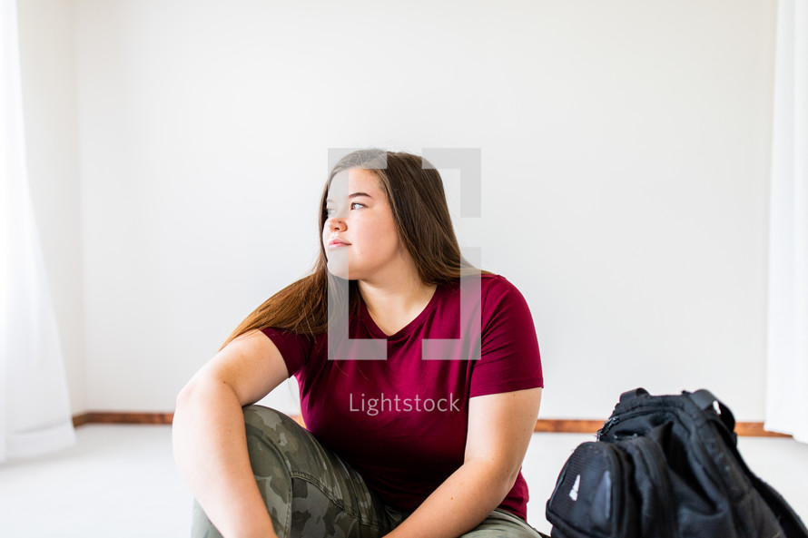 teen girl sitting next to a book bag 