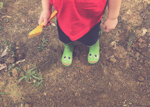 a toddler boy in rain boots playing in dirt 
