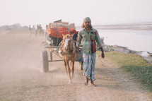 A man leading a horse pulling a wagon 