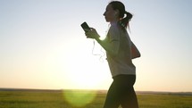 Young fitness sport woman running on road at sunset. Young woman runs in summer in park and listens to music with headphones. The concept of a healthy lifestyle.