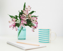 pencil on a spiral notebook, flowers in a vase, and mug