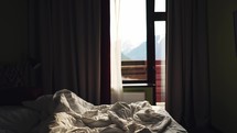 Unmade bed inside a hotel room. Morning scene with rumpled blanket and mountain view in the window.