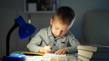 Children and education. Young boy Studying at desk in evening. Pretty little boy writing on a notebook. Young caucasian male child is very concentrated doing his homework at desk in his room.
