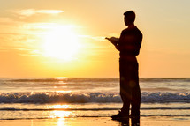 Man standing at the beach reading the Bible