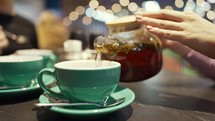 Tea Time. Person fills cup of tea in the restaurant. Close up. Woman pouring tea into a cup in coffee shop.