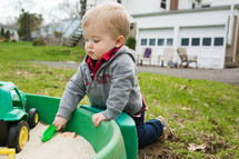 toddler boy playing in a sandbox 