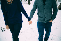 couple holding hands walking through snow 
