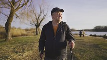 Senior man with trekking poles in their hands on the lake, Nordic walking, enjoy nature at sunset time.