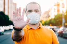 a man wearing a face mask standing in a city with his hand up saying stop 