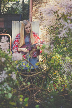 A woman playing a ukulele in a garden.