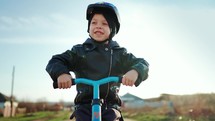 Cute little boy child wearing safety helmet learning to ride first balance bike in sunny day. Happy boy riding bike, having fun outdoors on sunset time. Active sport family concept. Slow motion 120fps