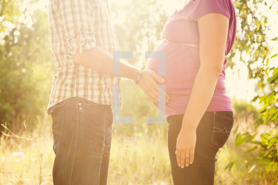Man touching pregnant woman's stomach while standing in a field.