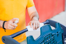 man cleaning a shopping cart with hand sanitizer 
