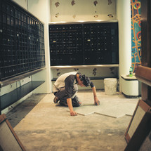 A construction worker puts down a tile floor in a post office.