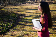 a girl standing in warm sunlight holding a notebook 
