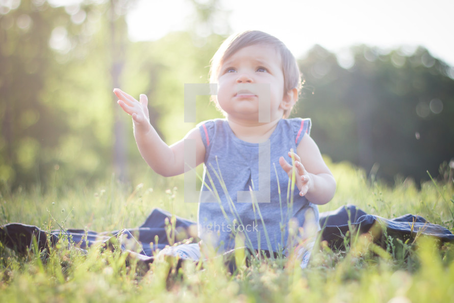 a toddler girl sitting in grass clapping her hands 