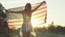 Young Woman Holds Up American Flag As She Walks Toward Camera in Slow Motion