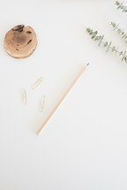 gold paper clips, pencil, wood, and twig on a desk 