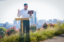 A man preaching a sermon on a hill overlooking a city.