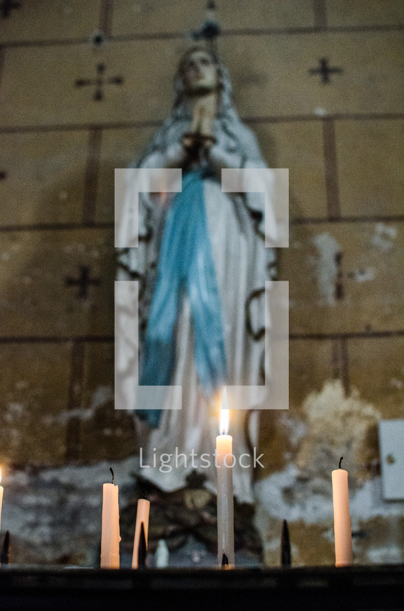candles in front of a praying statue of Mary 