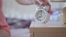 a woman waking up turning off an alarm clock 