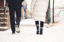 a man and woman walking on a sidewalk in the snow 