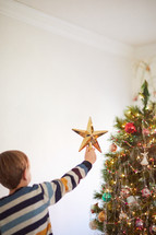 putting a star on top of a Christmas tree 