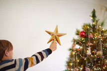 kid putting a star on top of a Christmas tree