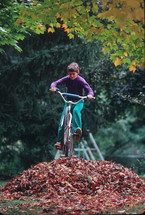 boy riding a bike through fall leaves 