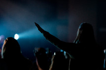 silhouettes of people in an audience at a concert with raised hands 