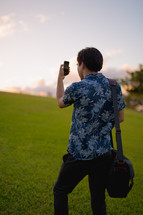 man in a Hawaiian shirt taking a picture with his cellphone 