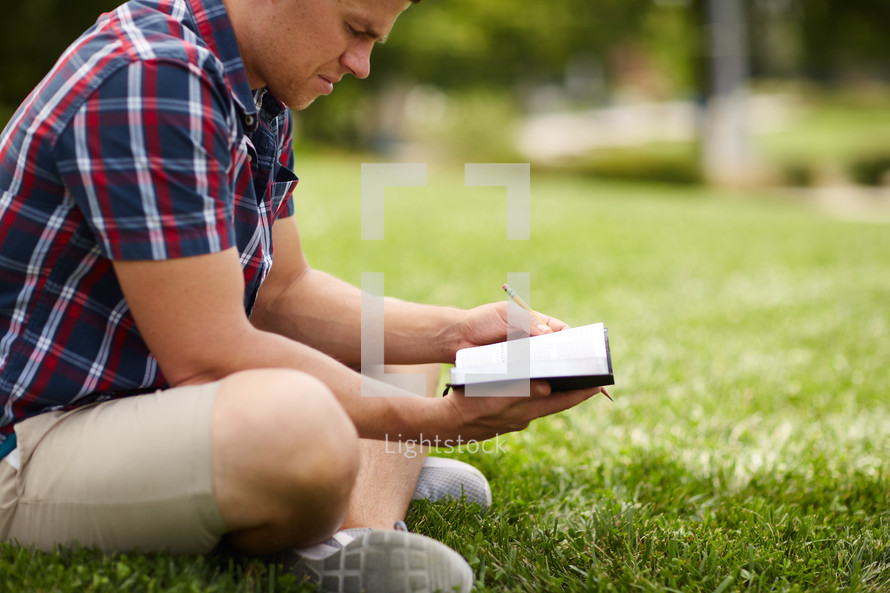 a person sitting in the grass reading a Bible 