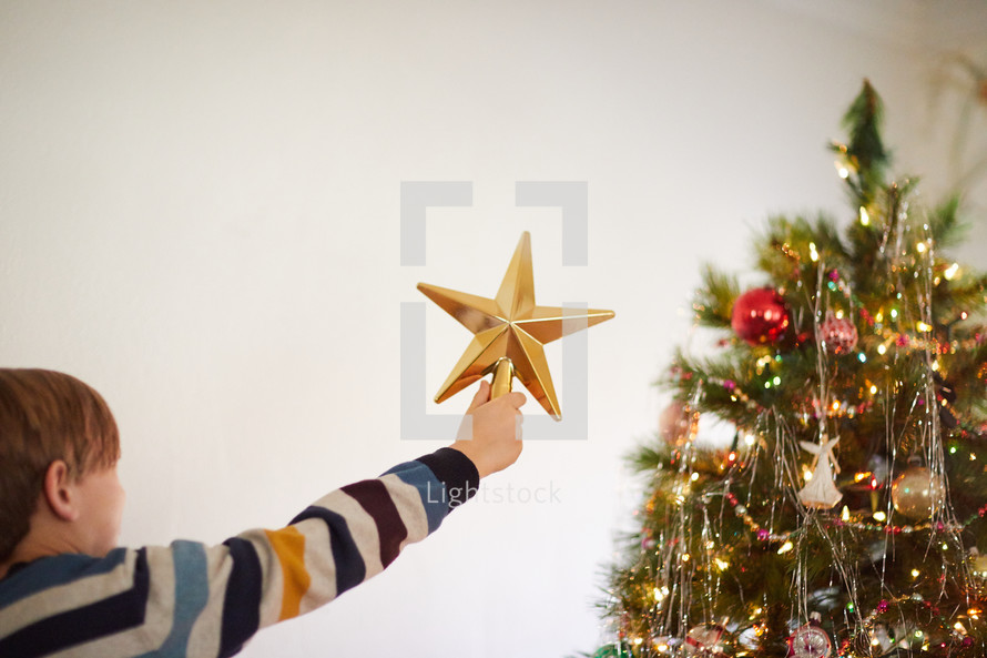 kid putting a star on top of a Christmas tree
