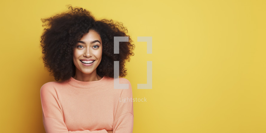 Joyful young woman with curly hair in a peach sweater, radiating happiness against a bright yellow background.