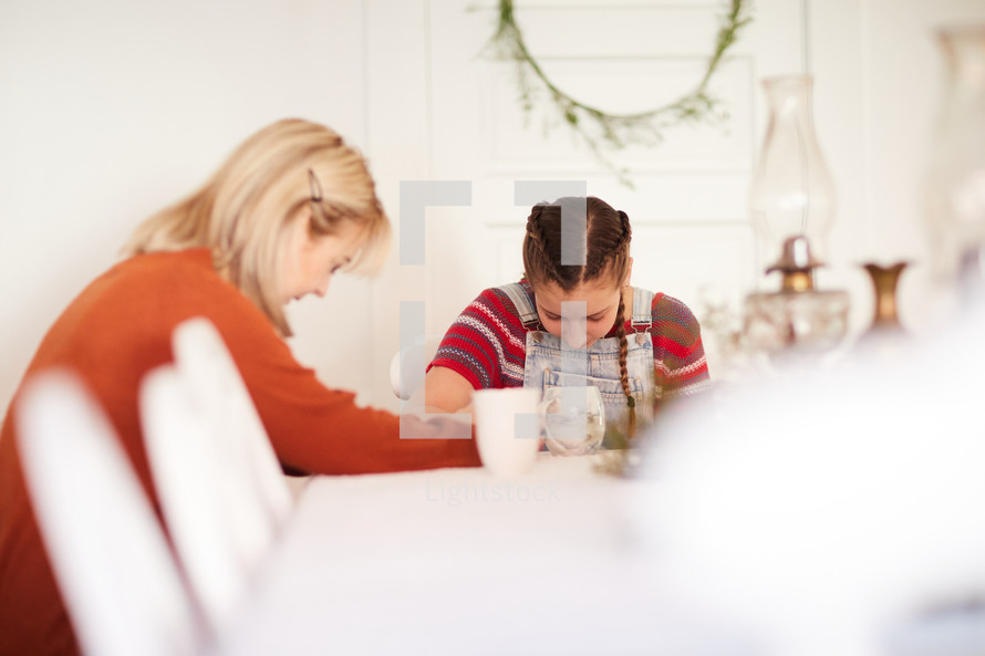 mother and daughter praying together at a table in the home