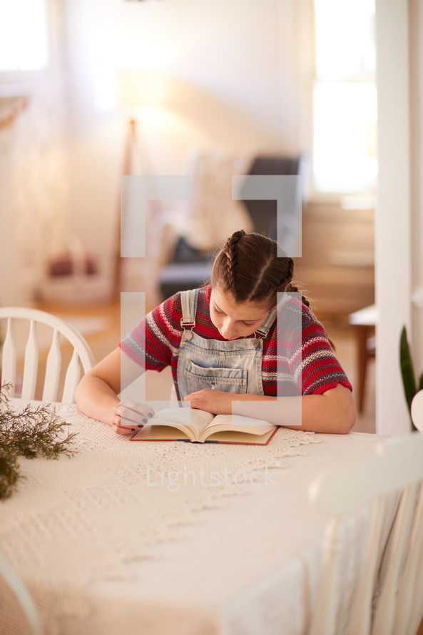 girl reading a book at a kitchen table 