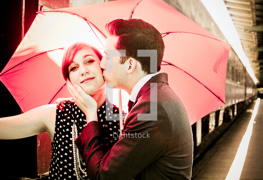 a couple kissing under a red umbrella near a train 