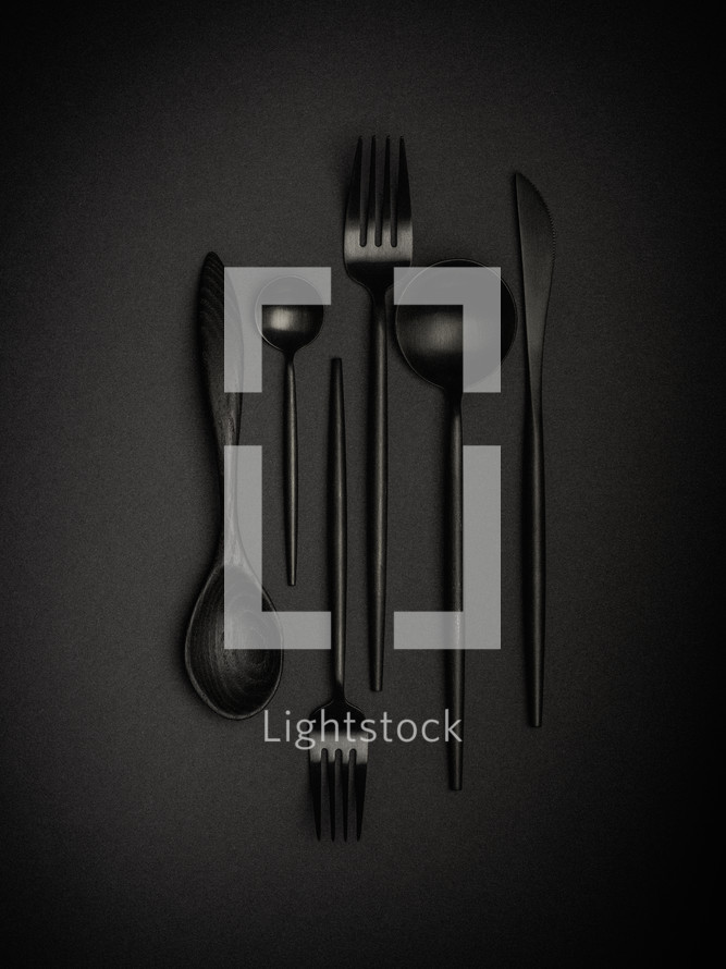 Black spoons, forks, and knives on a black background