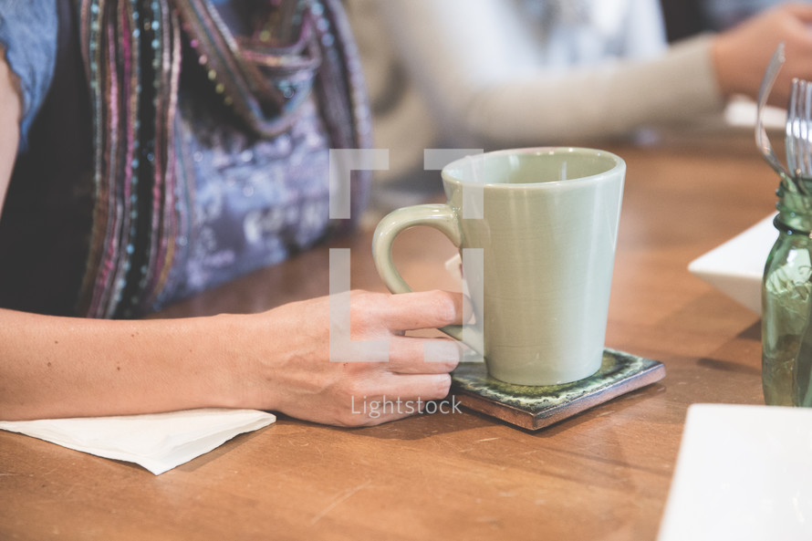 a woman sitting at a table with a mug of hot tea 