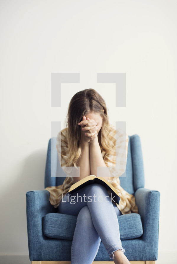 a woman sitting in a chair with head bowed praying 